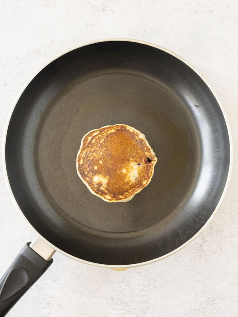 Dark skillet with cooked pancake on a light gray surface.