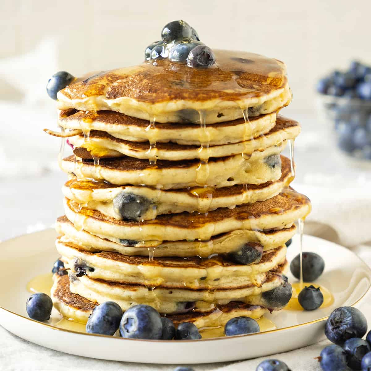 Tall stack of ricotta pancakes with blueberries and syrup. White plate and background. 