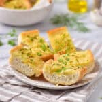 White plate with garlic bread pieces. Grey striped cloth and background.