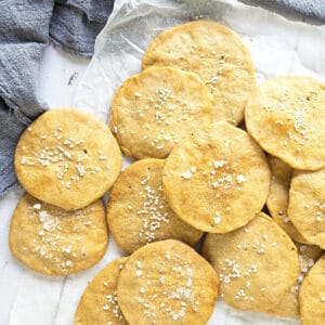 Pile of sea salt and sesame sprinkled round crackers. White paper, blue cloth.