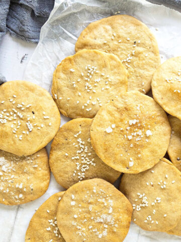 Pile of sea salt and sesame sprinkled round crackers. White paper, blue cloth.