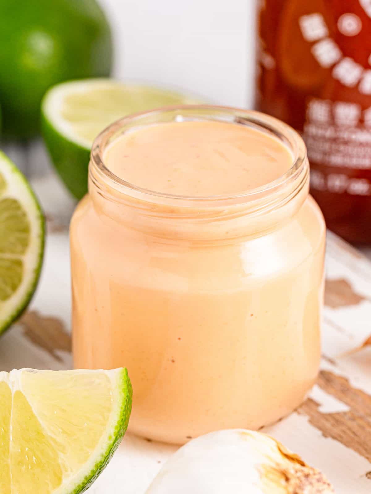 Open jar of spicy aioli. Lime wedges, white surface.