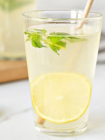 Glass of homemade lemonade with lemon slices and mint. Light gray background.