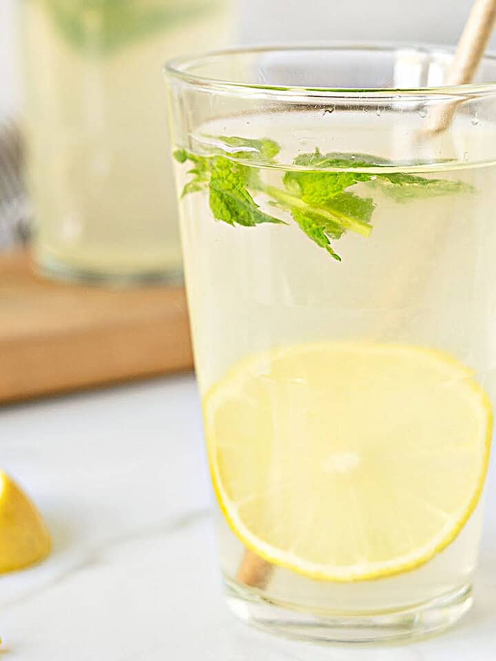 Glass of homemade lemonade with lemon slices and mint. Light gray background.