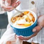 Holding a blue ramekin with peach cobbler. White background.