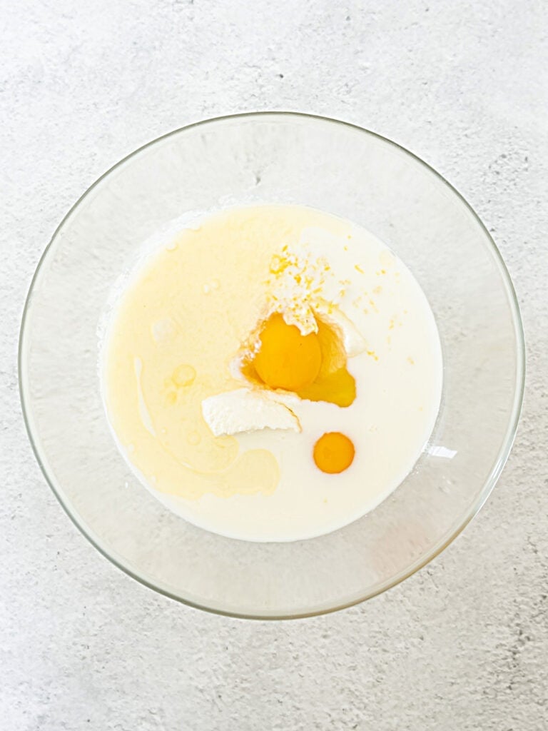 Egg, ricotta and milk in a glass bowl on a light gray surface.