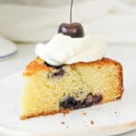 Cream topped cherry cake slice on a white plate. Close up image.