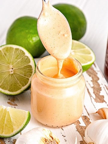 Easy spicy sriracha aioli in a jar and spoon. Limes, garlic, white background.