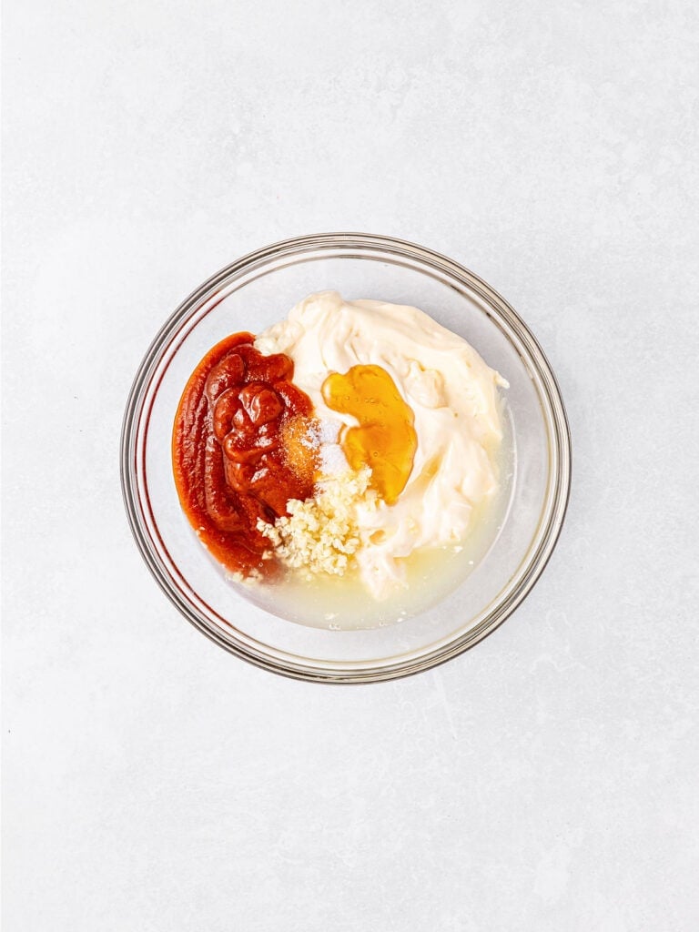 Glass bowl with ingredients for spicy aioli. White surface.