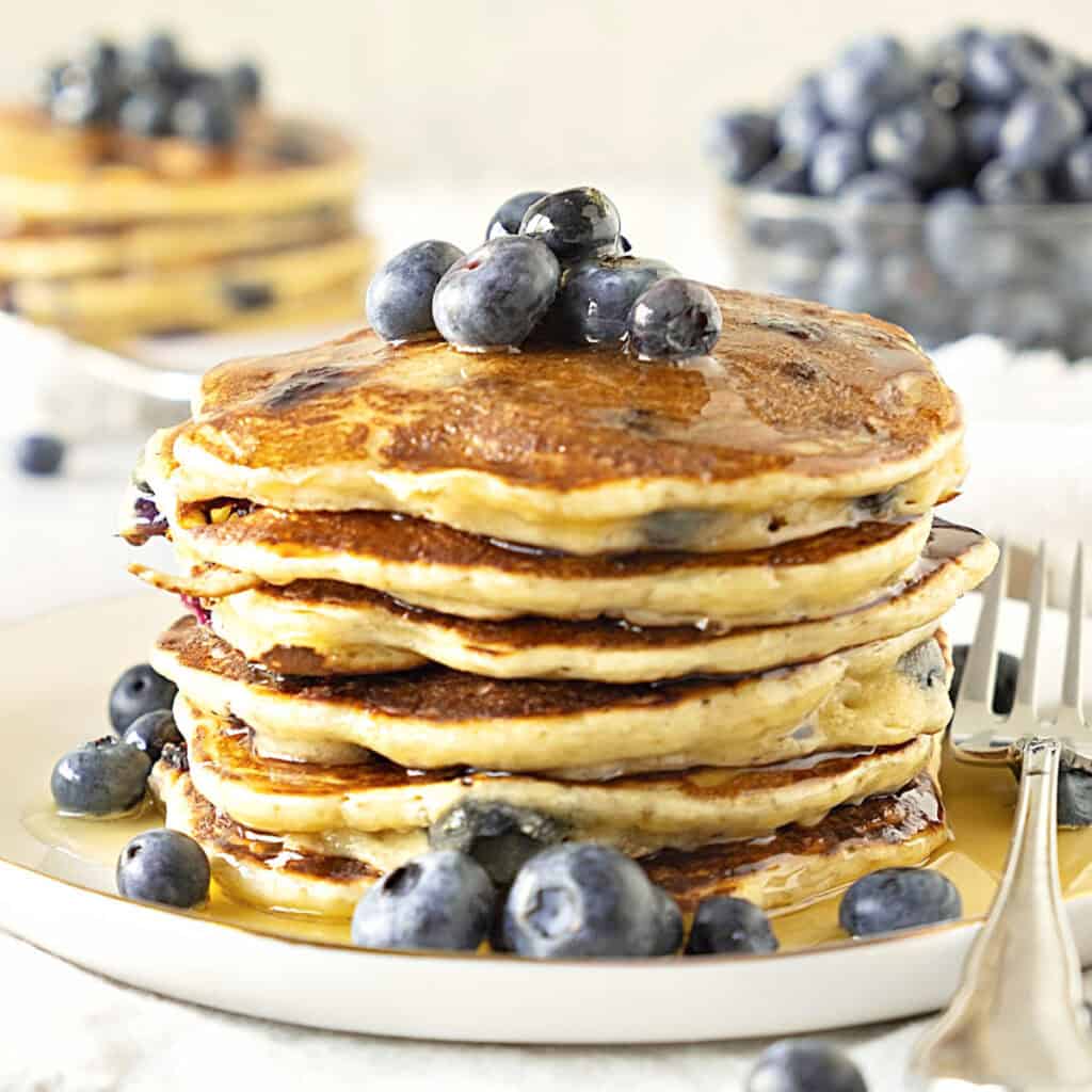 Close up stack of ricotta blueberry pancakes with syrup. White plate.