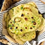 Pile of garlic herb naan in a basket with a blue striped cloth.