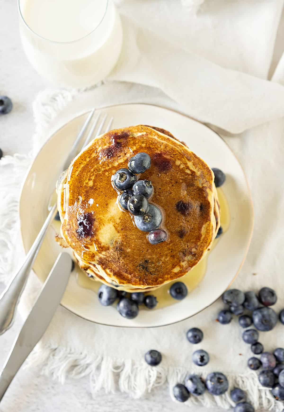 Top view of white plate with blueberry pancakes. White surface, loose blueberries.