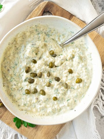 Top view of white bowl with tartar sauce on a wooden board. White cloth surface.