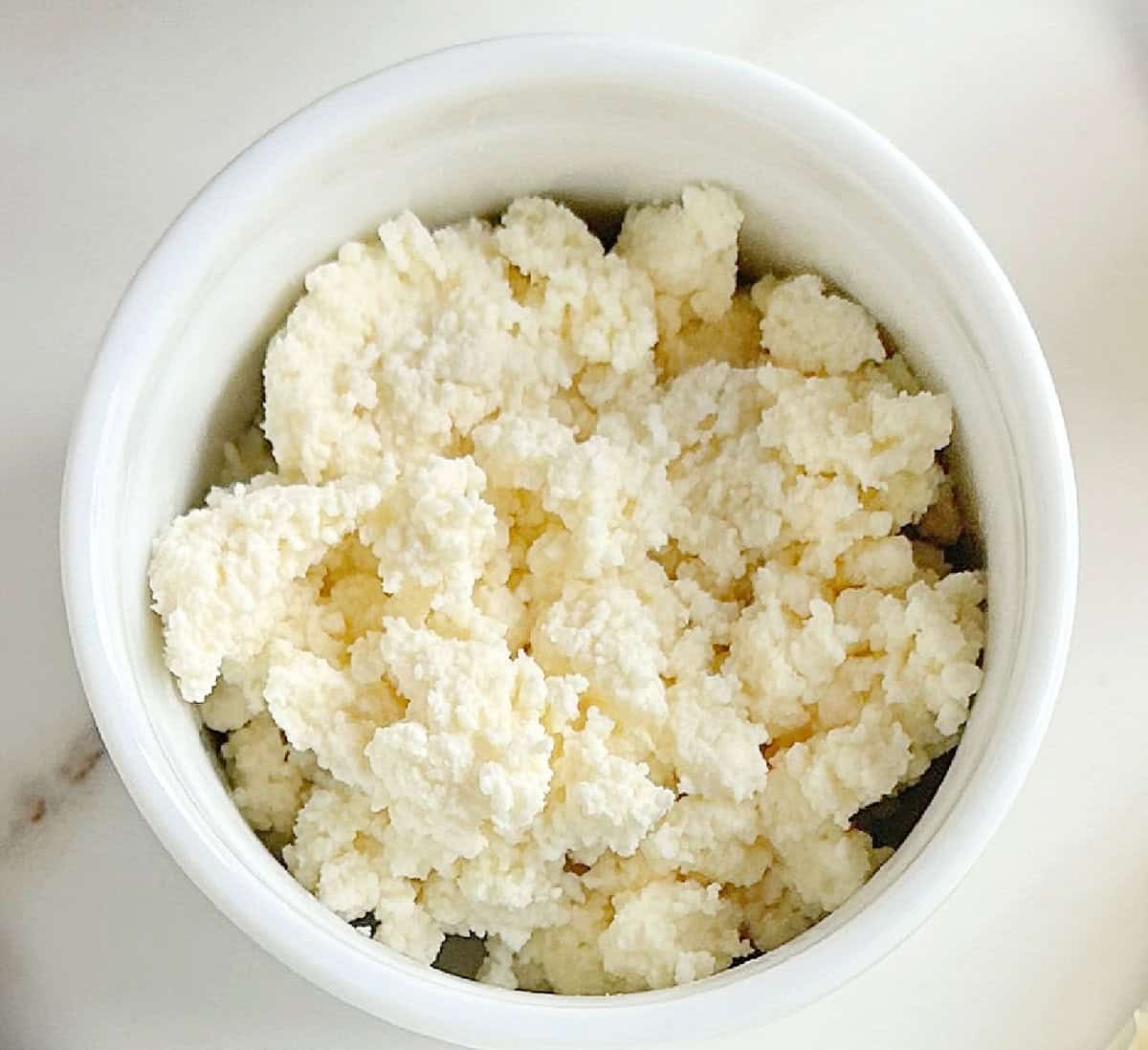 White bowl with ricotta cheese on a marbled surface.