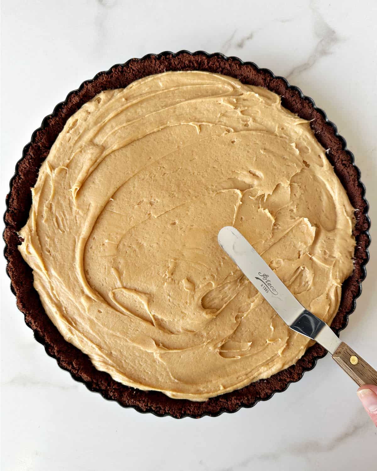 Spreading peanut butter filling on a chocolate crust with an offset spatula. White background. Top view.