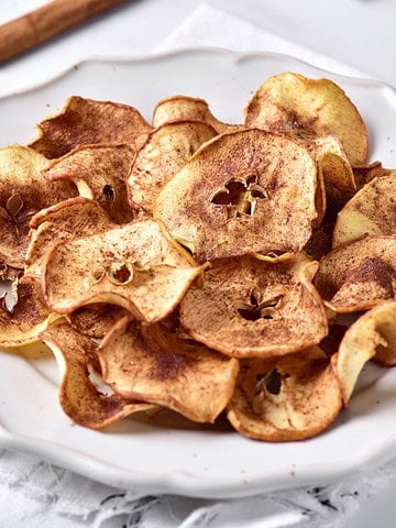 White plate with pile of cinnamon apple chips. White background.