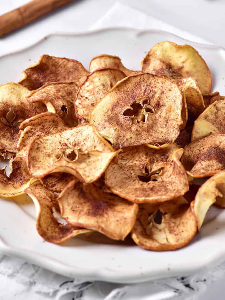 White plate with pile of cinnamon apple chips. White background.