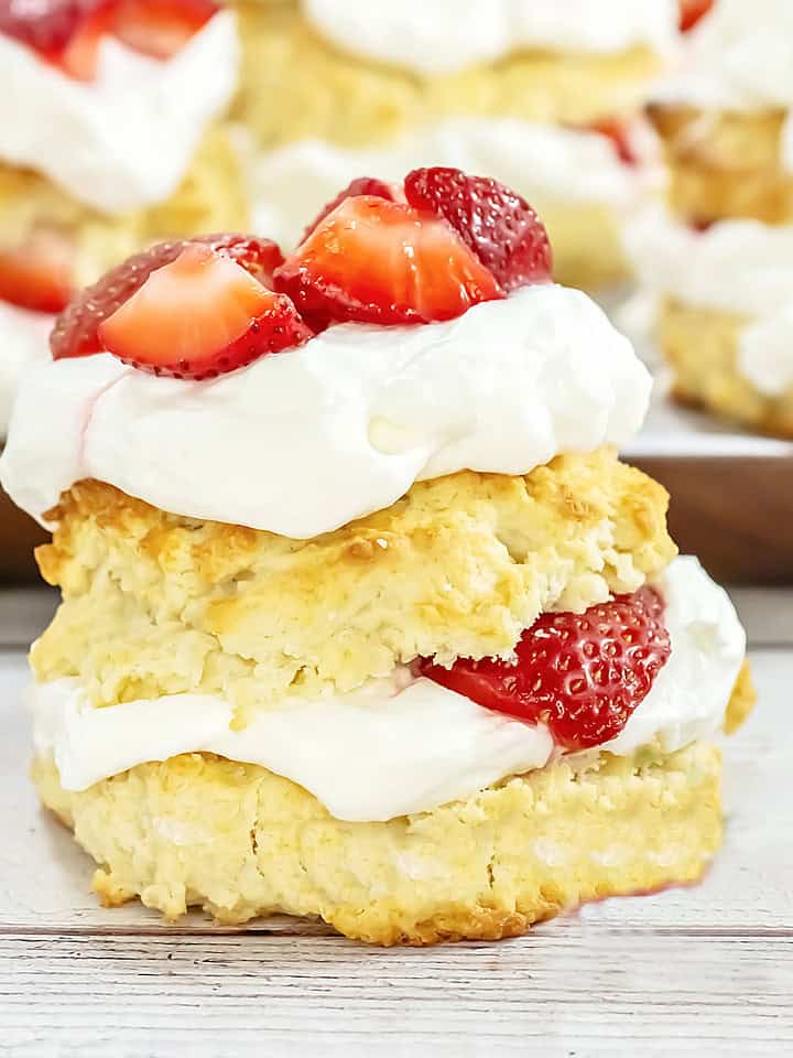 Close up fresh strawberry cream shortcake on a white wooden surface. More cakes in the background.