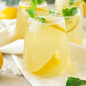 Close up of glass with ginger lemonade and mint sprig. Cream-colored cloth surface.