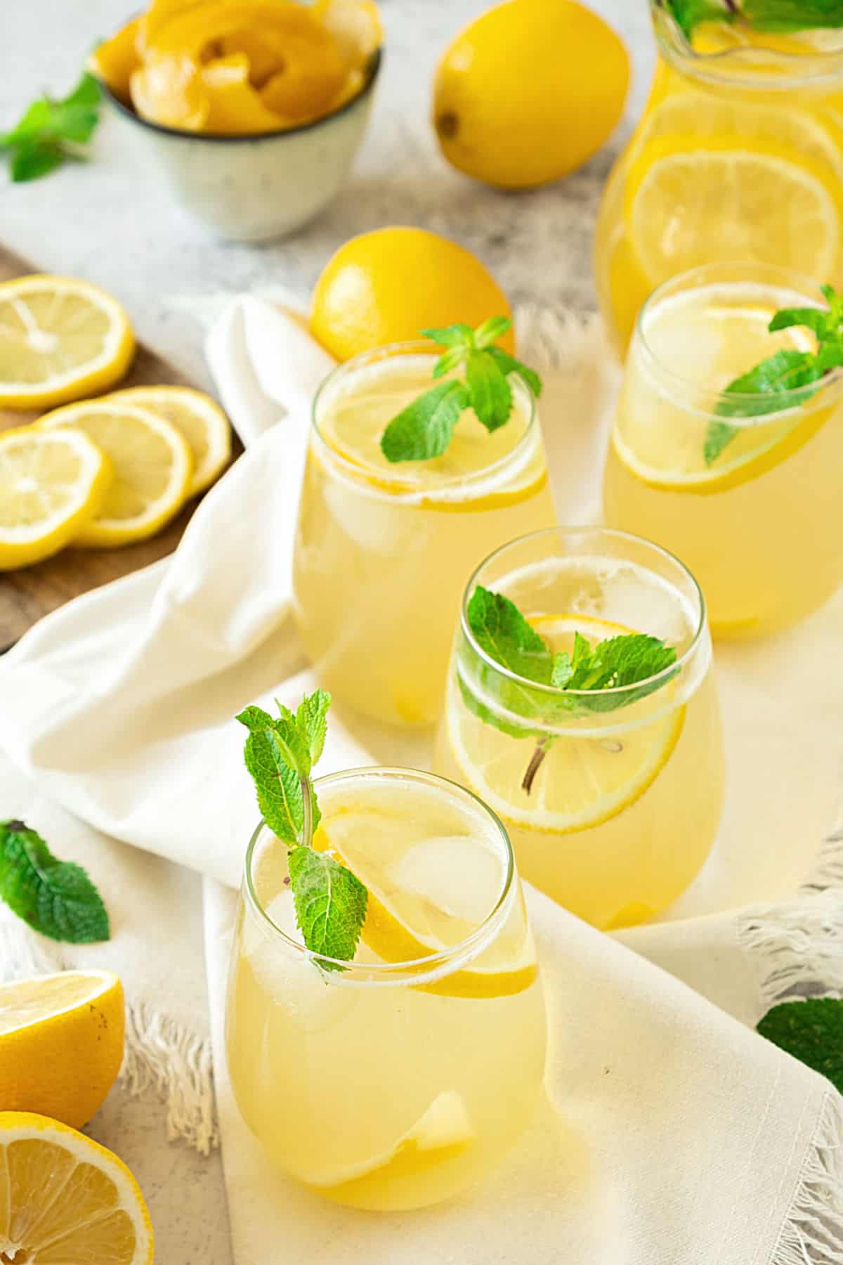 Several glasses of ginger lemonade and mint sprigs. White cloth, lemon slices in the background.