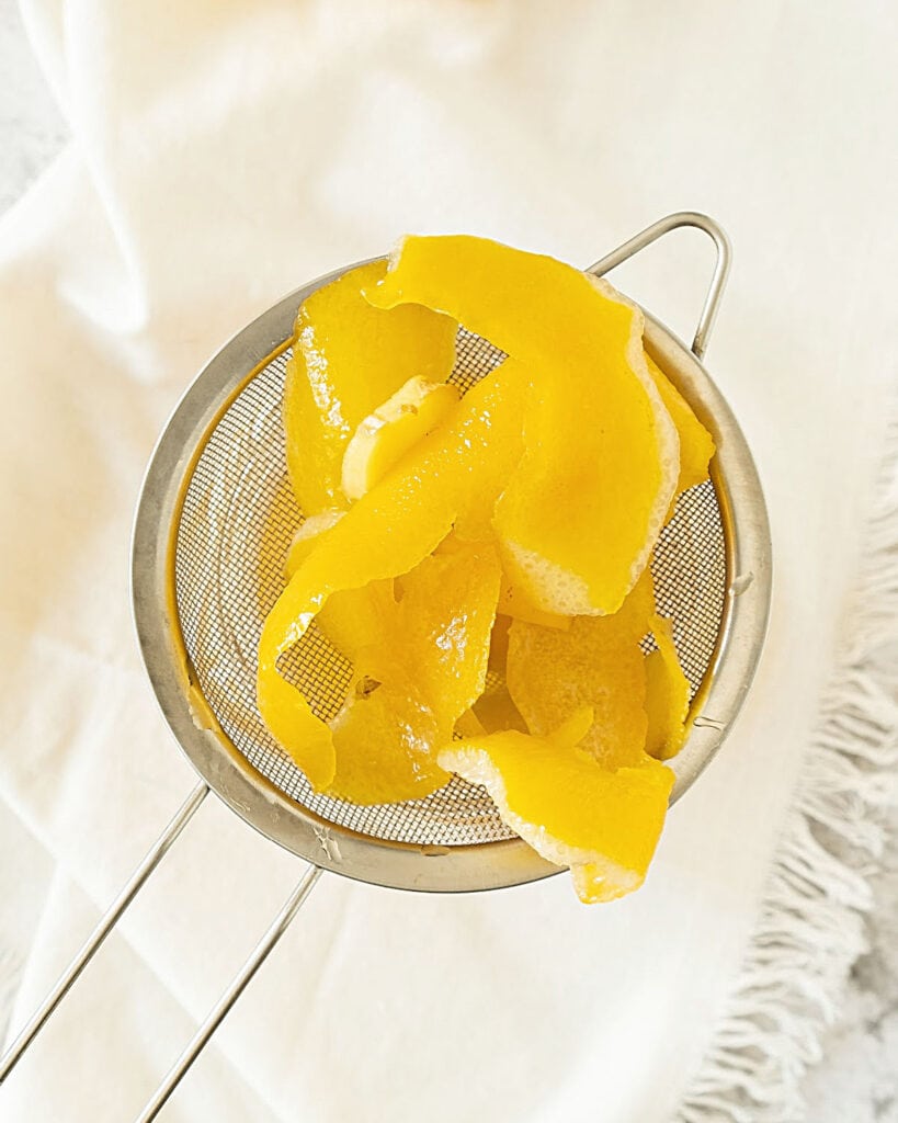 Metal colander with lemon peels. White cloth surface.