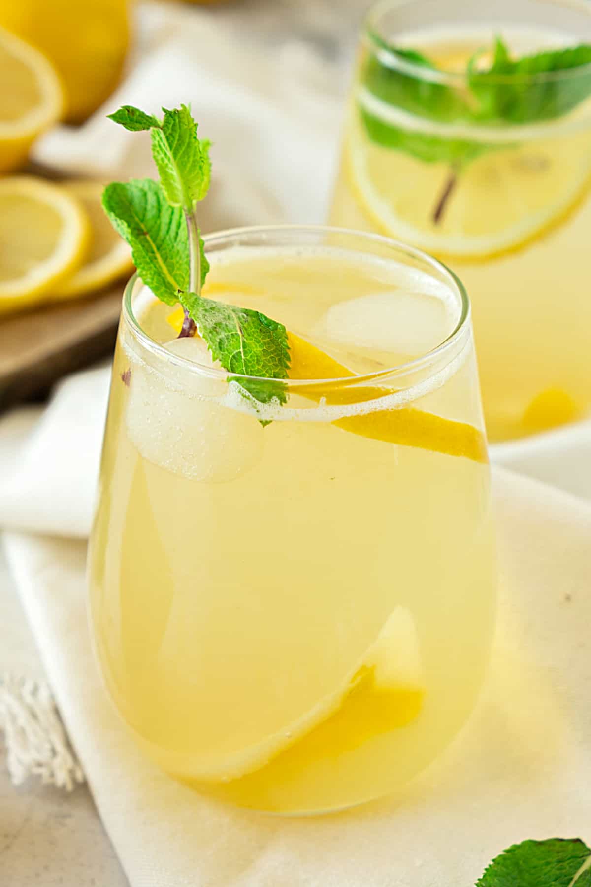 Glass of ginger lemonade. Cream-colored cloth surface, mint sprigs, lemon slices.