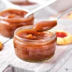 Spooning apple butter from a jar on a gray wooden board.
