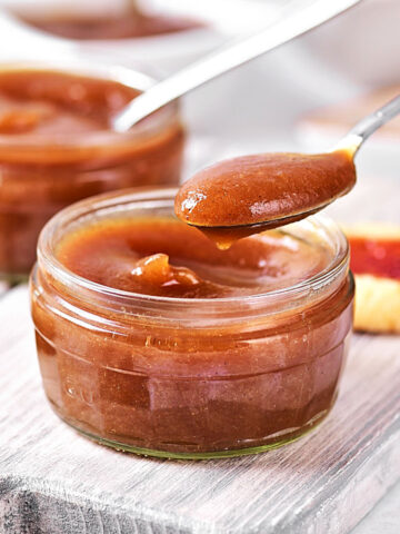 Spooning apple butter from a jar on a gray wooden board.