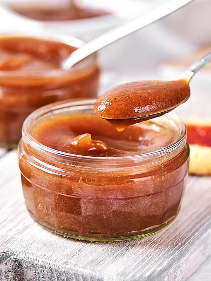 Spooning apple butter from a jar on a gray wooden board.