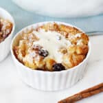Close up of white bowl of raisin bread pudding. Light blue background, white surface.