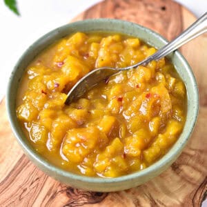 Greenish bowl with mango chutney and silver spoon. Wooden board surface.