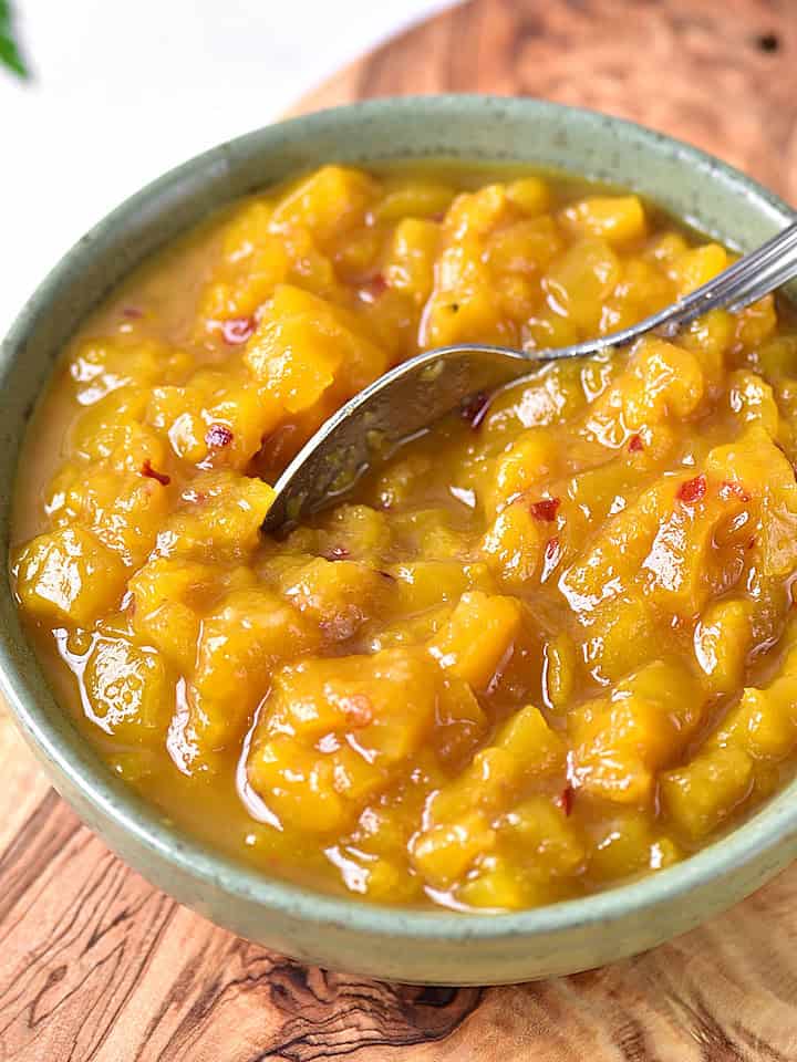 Greenish bowl with mango chutney and silver spoon. Wooden board surface.