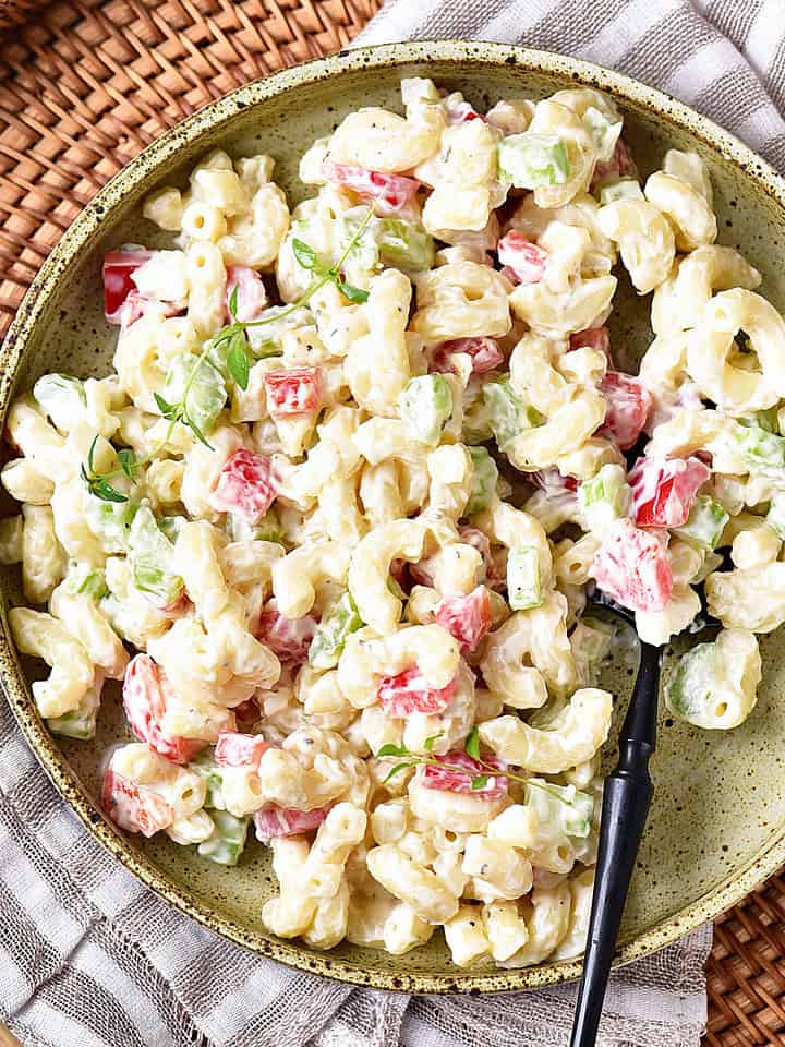 Top view of macaroni salad on a green plate. Striped cloth, basket tray.