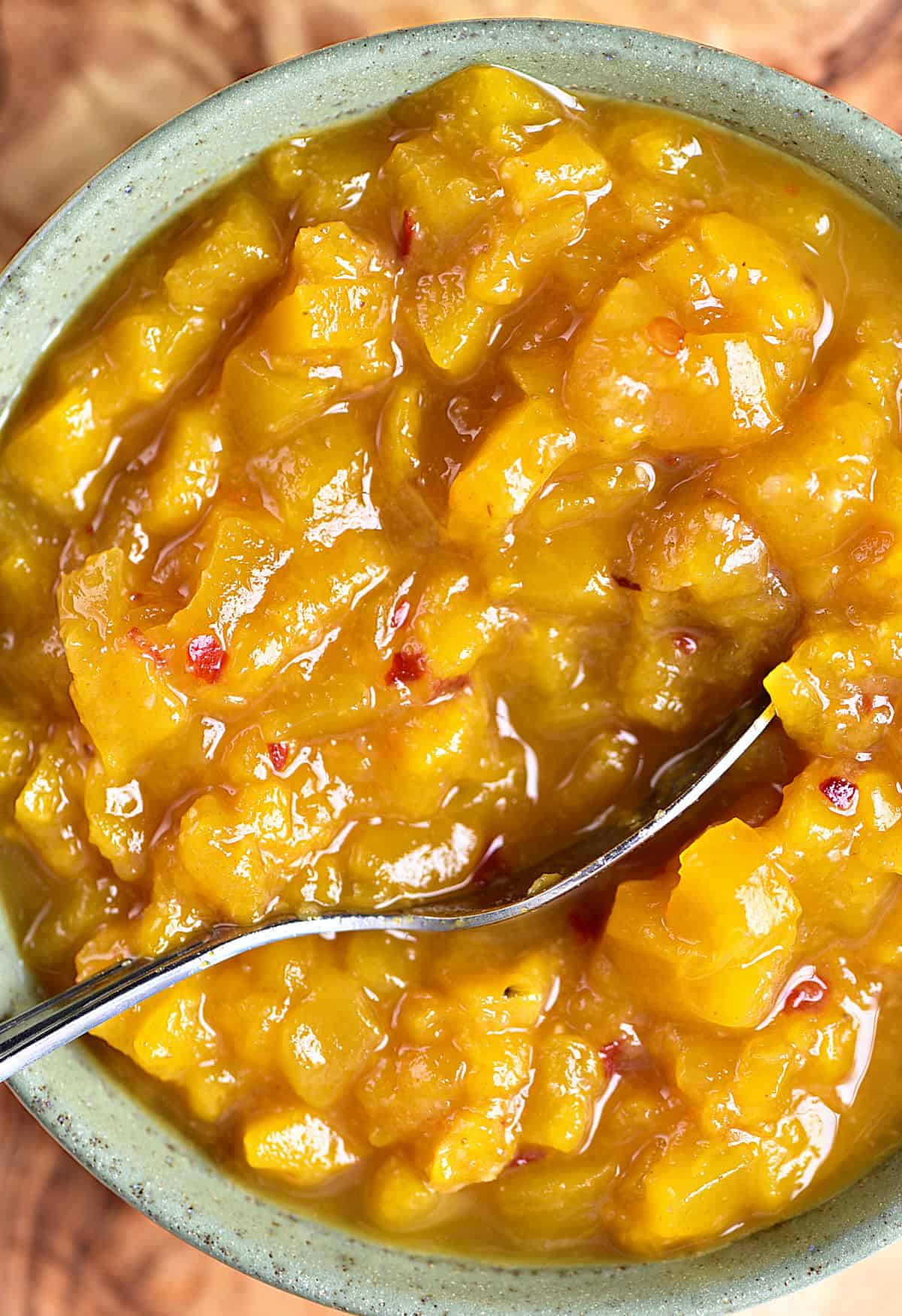 Close up image of mango chutney in a green bowl. Silver spoon.