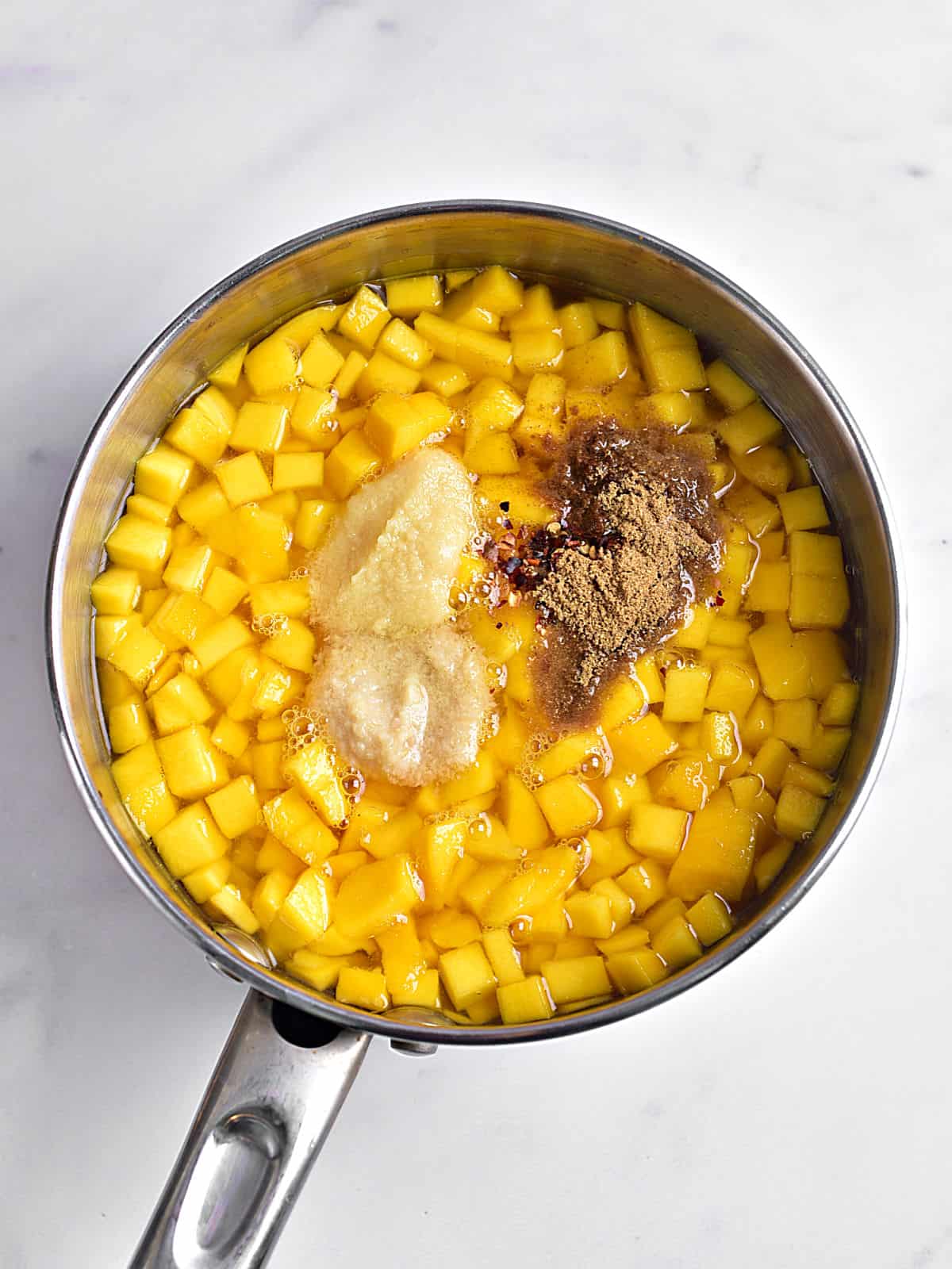 Metal saucepan with ingredients for mango chutney. Light gray surface.