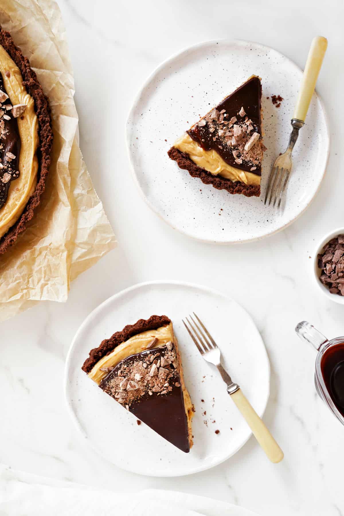 Top view of white plates with slices of peanut butter chocolate fudge tart. Forks, white surface. 