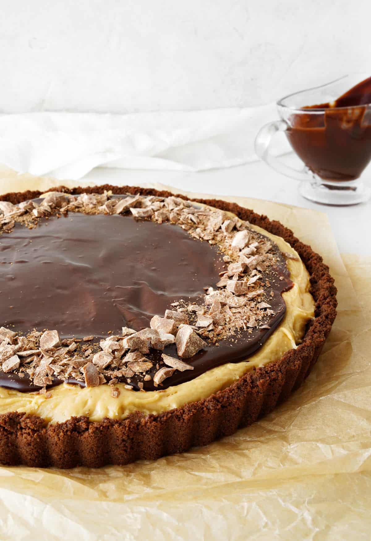 Partial view of chocolate sauce topped peanut butter pie on a beige paper. White background. 