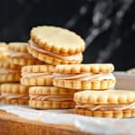 On a white paper, a pile of vanilla sandwich cookies. Dark background.