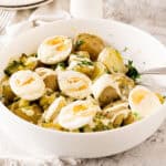 Close-up white bowl with potato egg parsley salad. White and light gray surface.