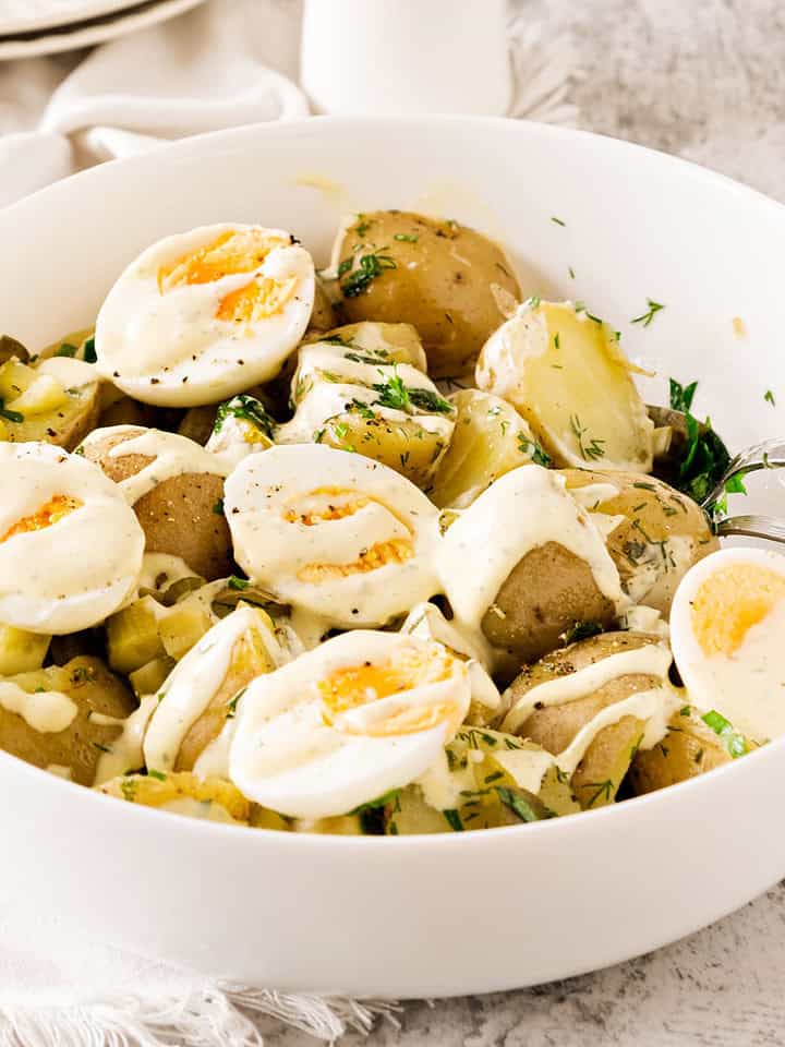 Close-up white bowl with potato egg parsley salad. White and light gray surface.