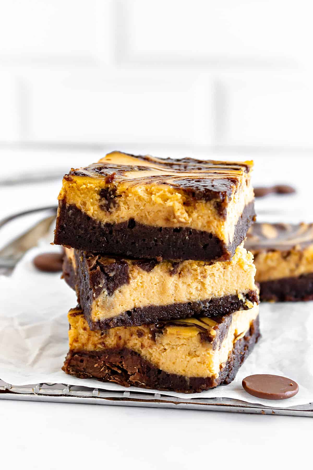 Stack of pumpkin cheesecake brownies on white paper. White tile background. 