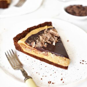 Peanut butter chocolate fudge tart on a white plate. Silver fork, white background.