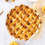 Baked peach cobbler with pie crust on a white round dish. Light gray background. Top view.