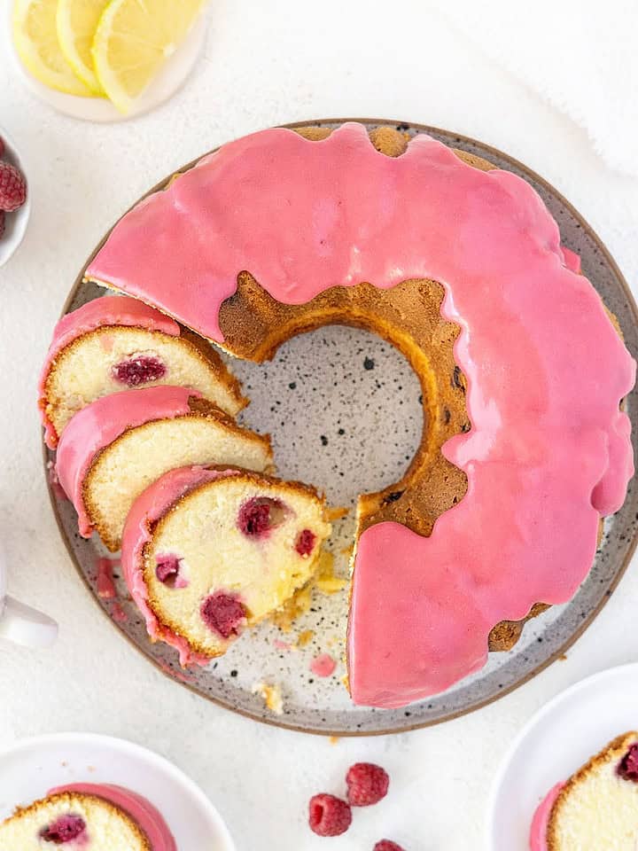 Glazed raspberry bundt cake on a white surface. Lemon slices, fresh berries.