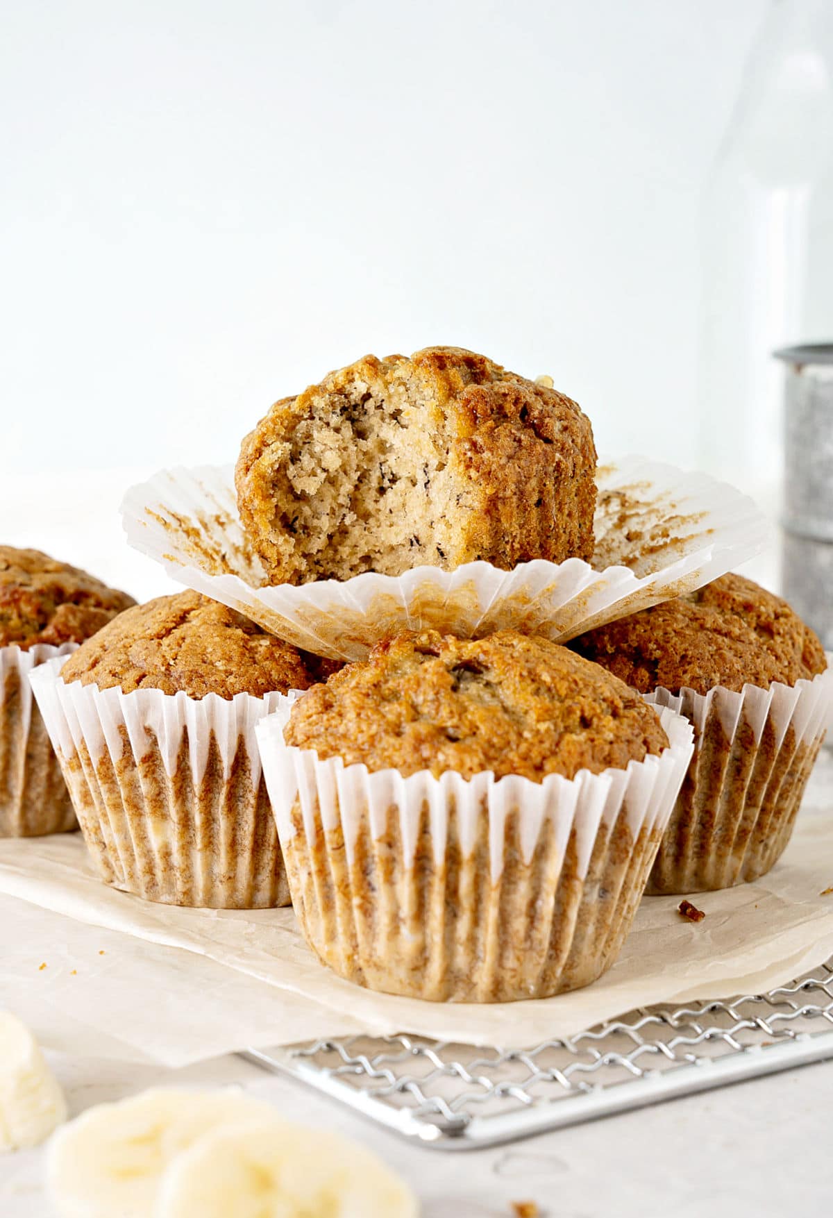 Several banana muffins in paper liners. Top one is bitten. Light gray background.