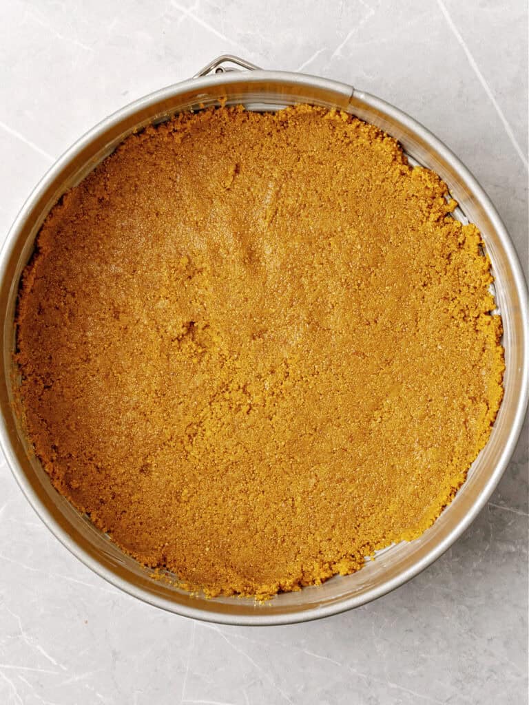 Round cake pan with cheesecake crust. Light gray surface. Top view.