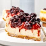 Close up slice of cherry-topped cheesecake. White plate, gray background.