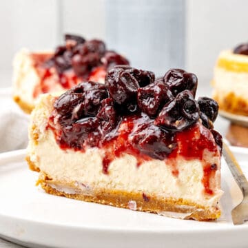 Close up slice of cherry-topped cheesecake. White plate, gray background.