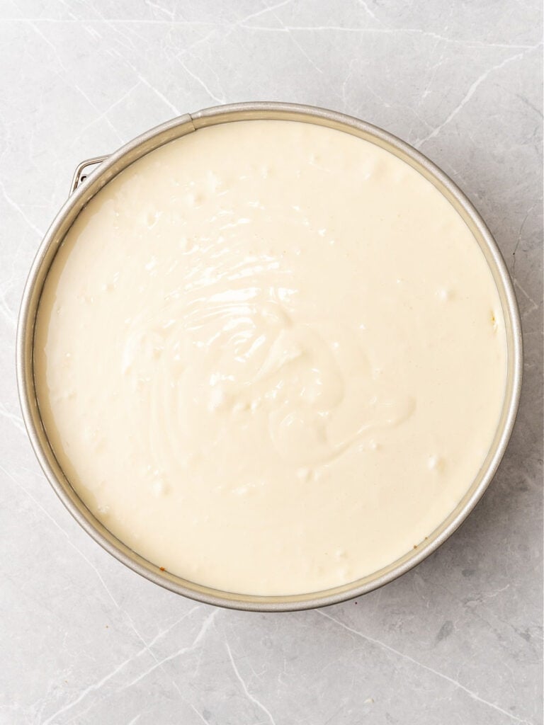 Cake pan with cheesecake batter. Light gray surface. Top view.