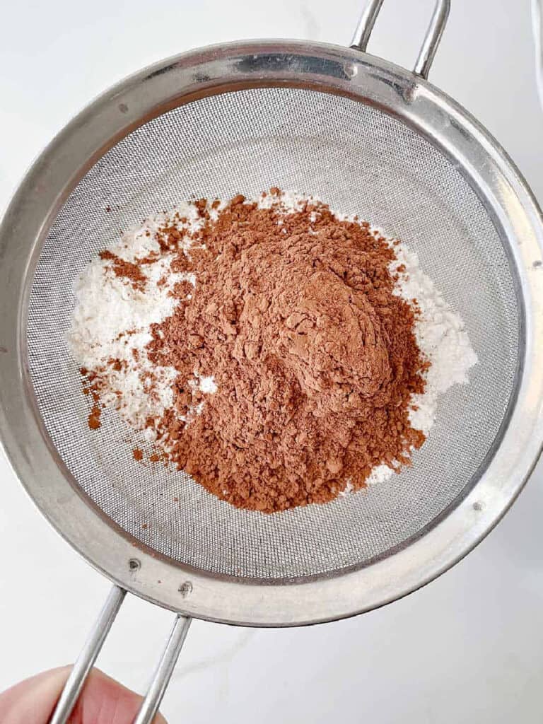 Metal sifter with cocoa powder and flour. White background. Top view.